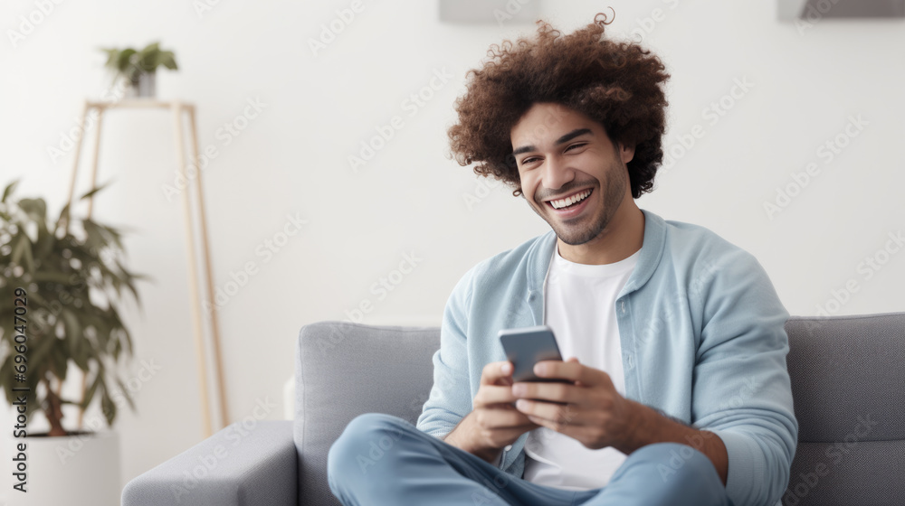 A man sits on the couch at home and smiles holding his smartphone in his hands A man sits on the couch at home and smiles holding his smartphone in his hands