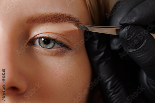 The master makes the client eyebrow correction with tweezers. photo