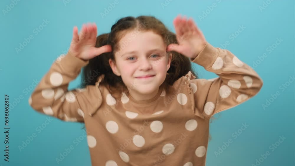 Portrait of funny cute preteen girl kid sticking out tongue and grimacing looking at camera, holding hands near temples, posing isolated over blue color background wall in studio. Misbehavior concept Portrait of funny cute preteen girl kid sticking out tongue and grimacing looking at camera, holding hands near temples, posing isolated over blue color background wall in studio. Misbehavior concept