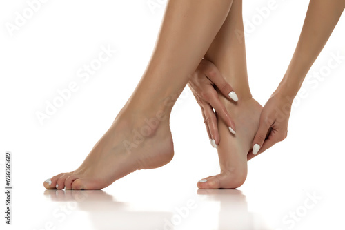 Woman is gently massaging and applying lotion to her bare feet, promoting self-care, relaxation, and foot skincare. Close up on a white stdio background