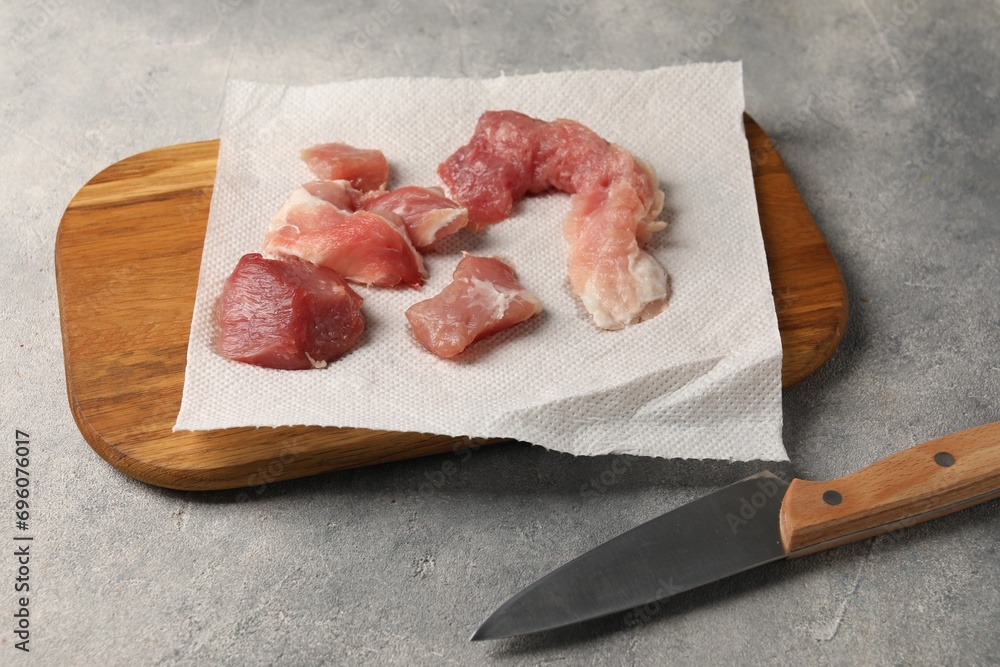 Paper towel, pieces of meat and knife on grey table