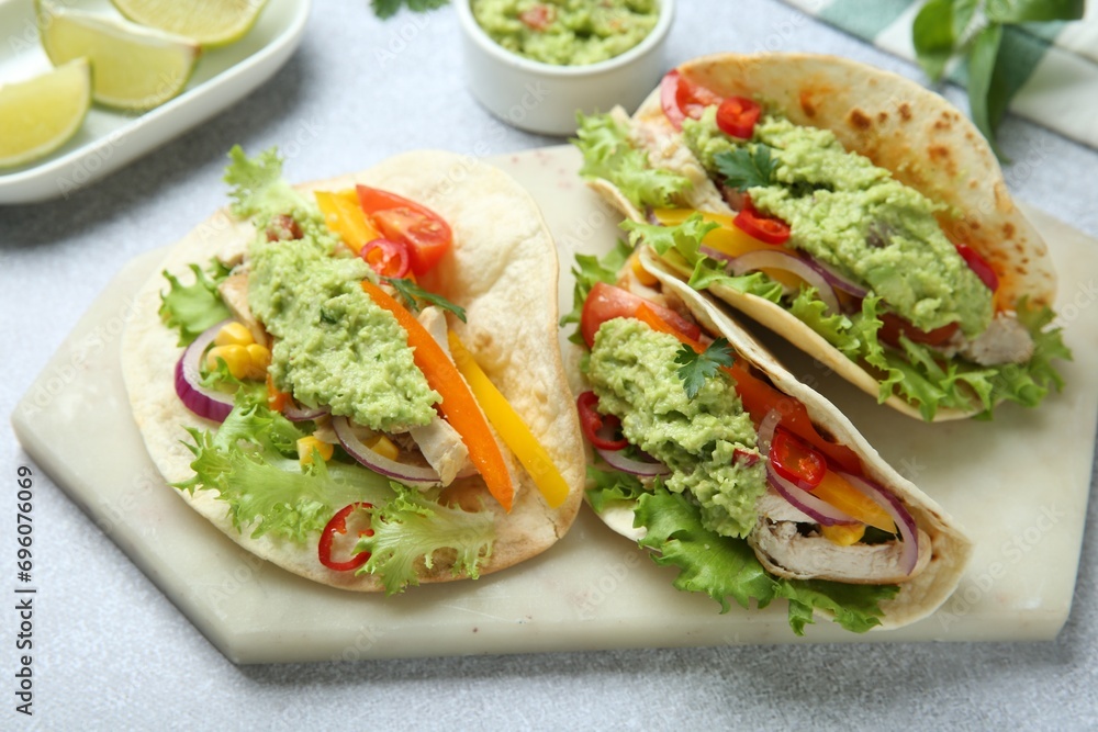 Delicious tacos with guacamole, meat and vegetables on light grey table, closeup Delicious tacos with guacamole, meat and vegetables on light grey table, closeup