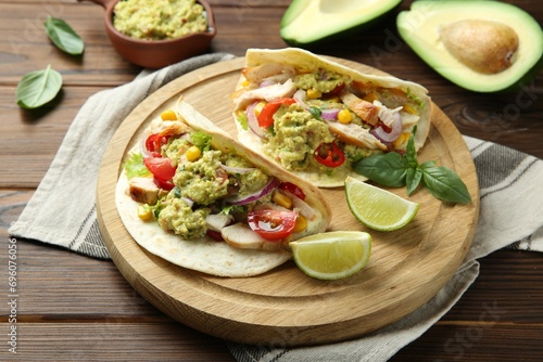 Delicious tacos with guacamole, meat and vegetables served with lime on wooden table