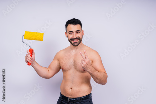 Cheerful young topless man hold paint roller isolated on grey background studio.