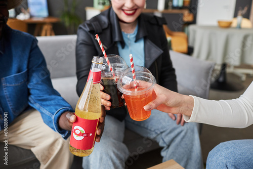 Close up shot of fizzy drinks in plastic cups and bottle in hands of diverse friends toasting at home