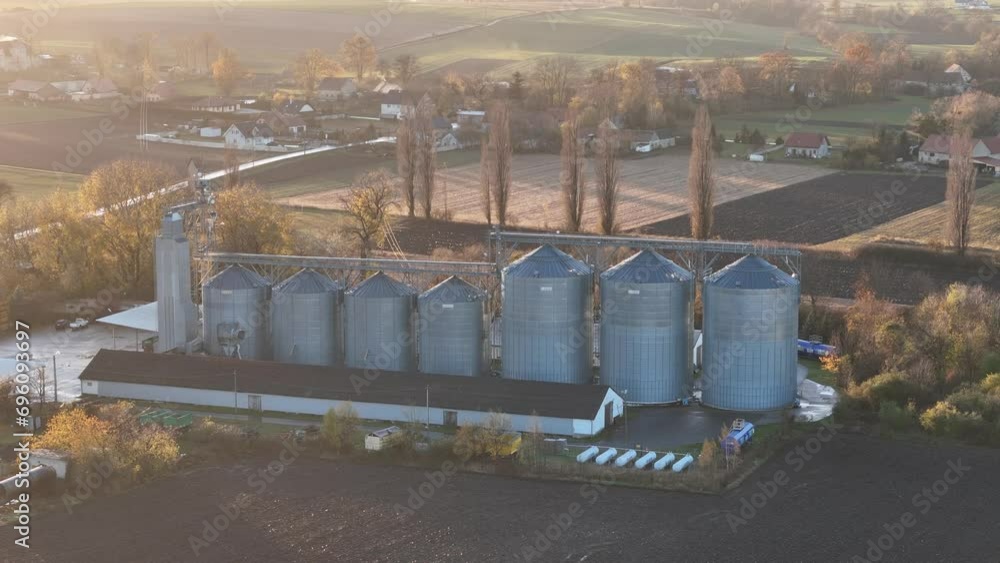 The sun sets over grain silos in a quaint village, casting a warm glow over the surrounding harvested lands. The sun sets over grain silos in a quaint village, casting a warm glow over the surrounding harvested lands.