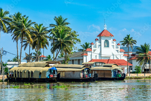 Old colonial Saint Thomas catholic church on the coast of Pamba river, with palms and anchored houseboats, Alleppey, Kerala, South India photo