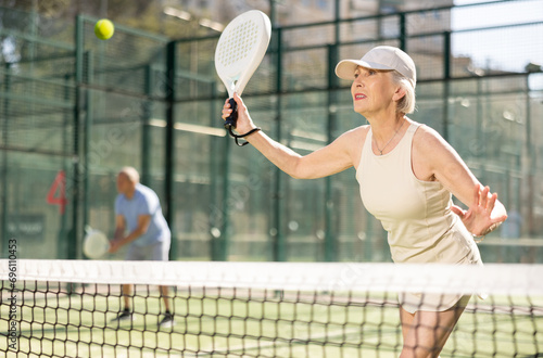 Mature sporty woman playing padel game in court on sunny day