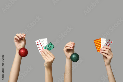 Female hands holding pills in blister packs and Christmas baubles on grey background photo