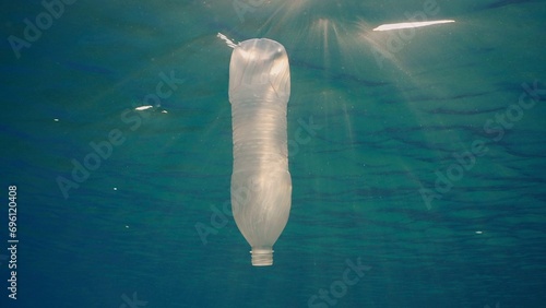 Disposable plastic bottle drift under surface of water in bright sunrays. A plastic bottle is thrown into the sea slowly drifts in water column in rays of morning sun, Red sea, Egypt, Africa photo