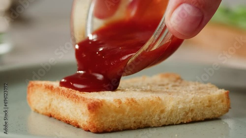 Adding red sauce jam on fried bread close-up. Cooking sandwich at cafe. Pouring tomato sauce on top. Food concept photo