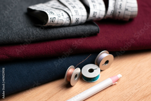 texture of dark red, dark blue and dark gray fabrics, white pencil, spools and plastic meter of threads on a wooden table
