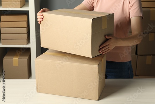 Packaging goods. Woman with cardboard boxes at white table indoors, closeup © New Africa