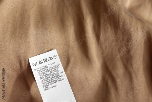 Clothing label in different languages on beige garment, closeup photo