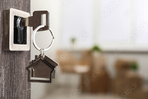 Mortgage and real estate. Open door with key and house shaped keychain against blurred background, space for text