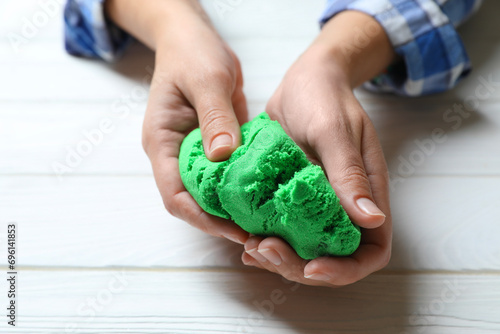 Woman playing with green kinetic sand at white wooden table, closeup