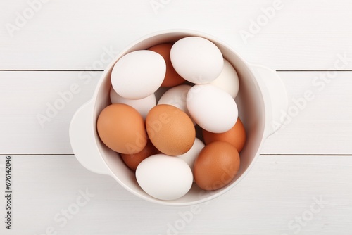 Unpeeled boiled eggs in saucepan on white wooden table, top view