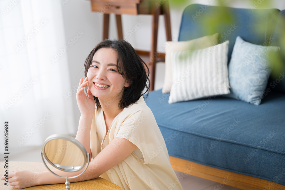 Closeup of a young, pretty woman with an enraptured smile checking her skin tone and makeup in the mirror With green front blur of houseplants Closeup of a young, pretty woman with an enraptured smile checking her skin tone and makeup in the mirror With green front blur of houseplants