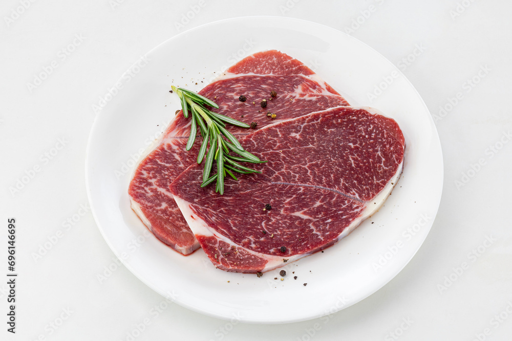 a plate of beef steaks with rosemary and peppercorns on white background.