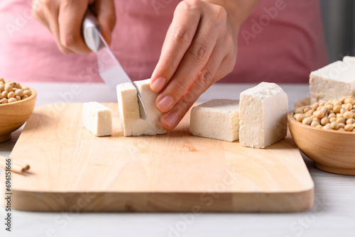 Hand holding knife and cutting tofu on wooden board, Healthy eating