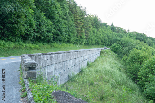 a stone automobile traffic bridge cut into the side of a mountain, the single lane, two-way roadway brings traffic over some foothills and through a valley for interstate travel of people and goods