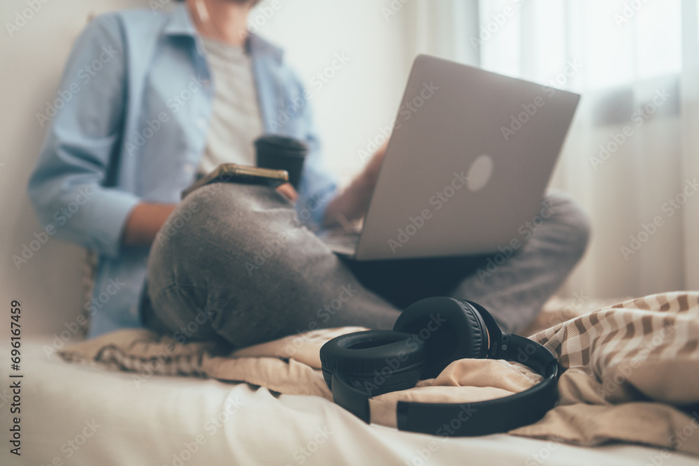 Fototapeta premium Focus on headphone. People sitting on bed holding coffee glass and using computer laptop. Freelancer working online at home. Meeting video conference with customer or connecting with social network