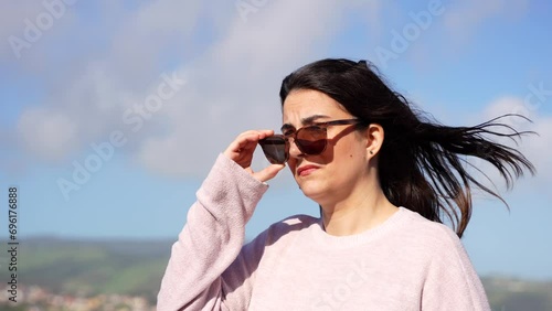 Woman wearing sunglasses being dazzled by the sun in a windy day, handheld shot