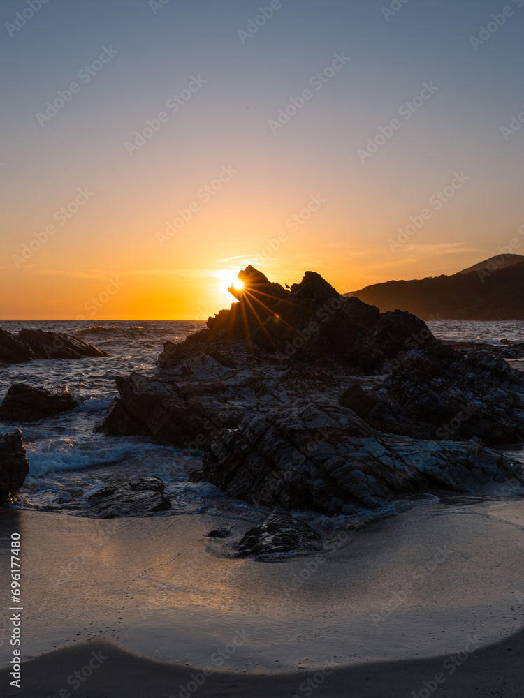 Sunlight star behind rock formation on the beach.