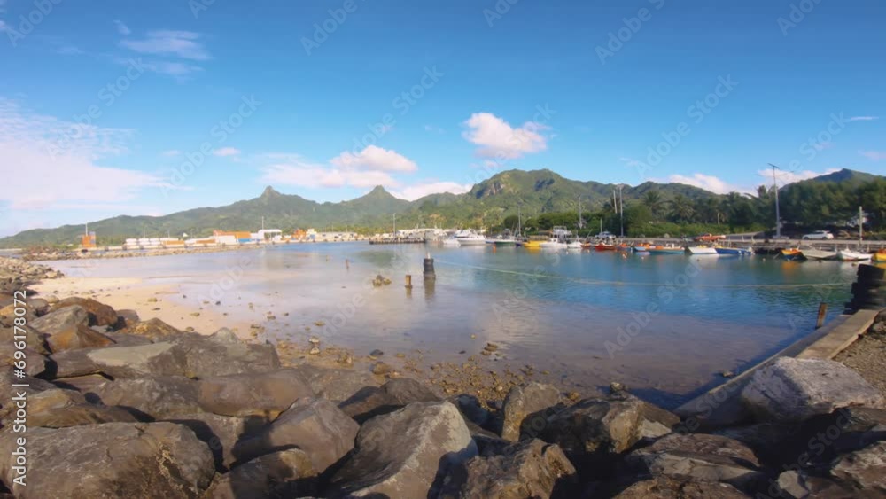 Still view of sandy rocky bay area in Avatiu Harbor look out to boats transportation ships with buildings and Jurassic park like mountains far background during good weathered day blue sky Still view of sandy rocky bay area in Avatiu Harbor look out to boats transportation ships with buildings and Jurassic park like mountains far background during good weathered day blue sky