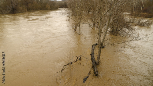 Muddy water in the river during heavy spring or autumn rains. A flooded plain with trees and shrubs. Bad weather. A natural disaster.