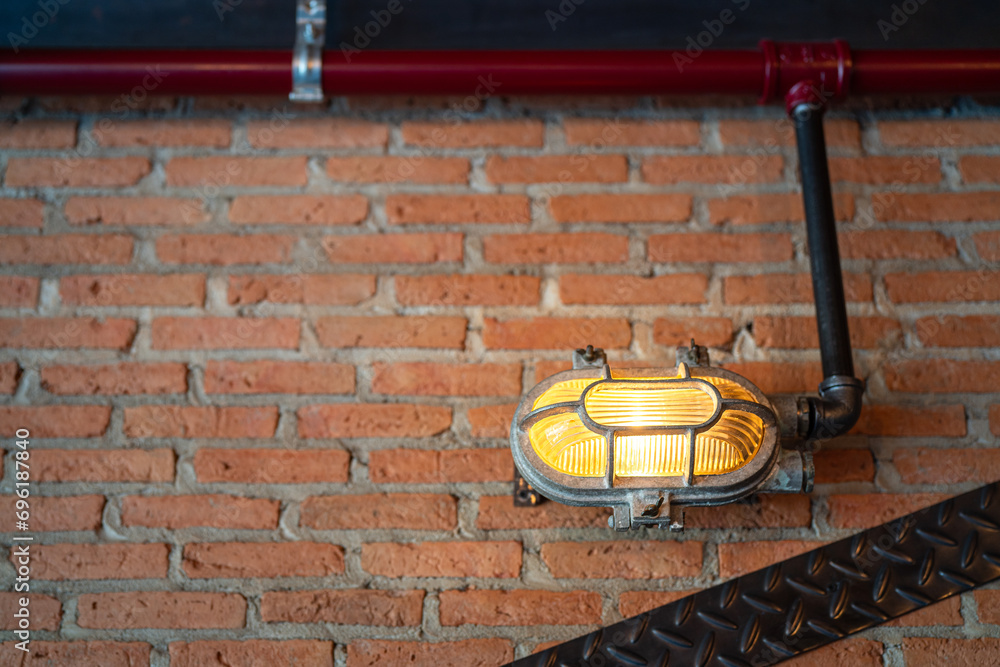 An industrial-loft designed lighting lamp with metal cover that installed on brick wall with iron tube cable line. Interior decoration object photo. Close-up and selective focus.
