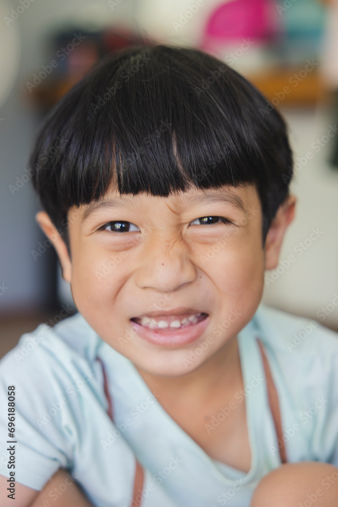 Close up portrait of Asian boy with black bangs, black eyes with a smiling face wearing a light green shirt look at camera and sitting on the floor of his house and hand holding pencil to draw. Close up portrait of Asian boy with black bangs, black eyes with a smiling face wearing a light green shirt look at camera and sitting on the floor of his house and hand holding pencil to draw.