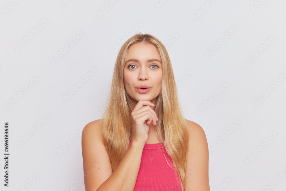 Pretty woman with blue eyes in pink top against white background, touching her chin with smile, happy life concept, copy space Pretty woman with blue eyes in pink top against white background, touching her chin with smile, happy life concept, copy space