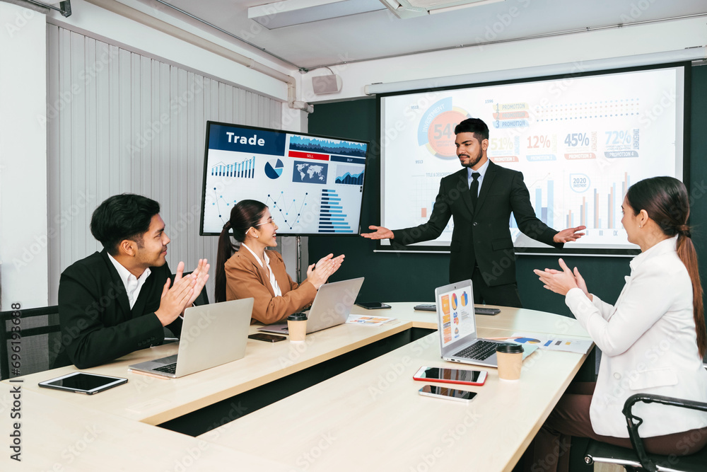 Fototapeta premium A cheerful and confident Asian businessman stands, presenting bar charts data from the projector screen to his office colleagues. Asian businessman leader role at the meeting.