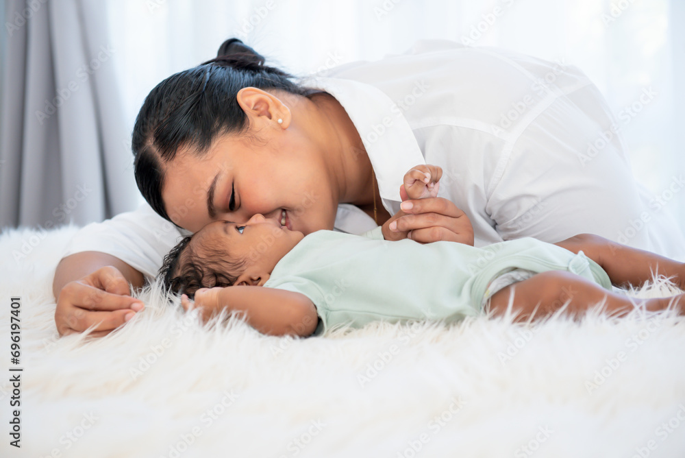 Asian mother kissing her 1-month-old baby newborn son, half Thai half Nigerian who is lying in white bed, with smile and happy, to relationship in family and infant concept. Asian mother kissing her 1-month-old baby newborn son, half Thai half Nigerian who is lying in white bed, with smile and happy, to relationship in family and infant concept.