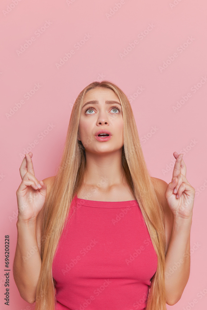 Closeup shot of pretty girl with long fair hair in pink top standing on pink background pointing up, good choice concept, copy space Closeup shot of pretty girl with long fair hair in pink top standing on pink background pointing up, good choice concept, copy space