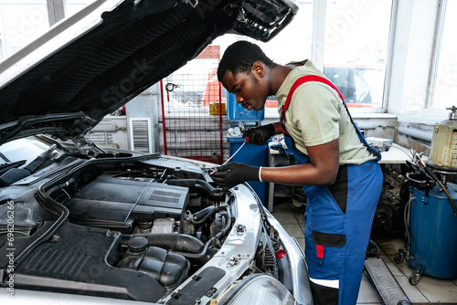 Young African man working under the hood of car fixing engine in auto service