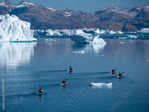 Fjord Landschaft in Grönland mit Kajaks und Eisbergen und im Hintergrund Berge