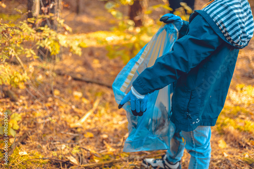 A child volunteer collects plastic waste in a garbage bag. A child eco activist saves the forest from plastic waste. Pollution of the planet with garbage, environmental problems. © Александр Лебедько