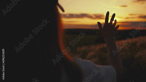 Girl looks at the sun through her hand at sunset. photo