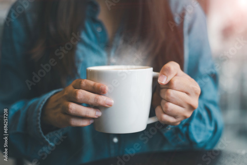 In the morning, a young woman holds a hot cup of tea or coffee in her hands.