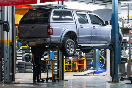 Pickup truck lifted into the air using a mechanical bridge jack in a service garage for car repair and maintenance at night time, back view