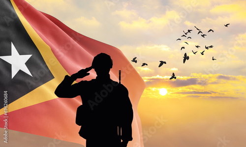 Silhouette of a soldier with the East Timor flag stands against the background of a sunset or sunrise. Concept of national holidays. Commemoration Day.