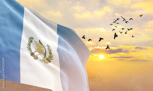 Waving flag of Guatemala against the background of a sunset or sunrise. Guatemala flag for Independence Day. The symbol of the state on wavy fabric. photo