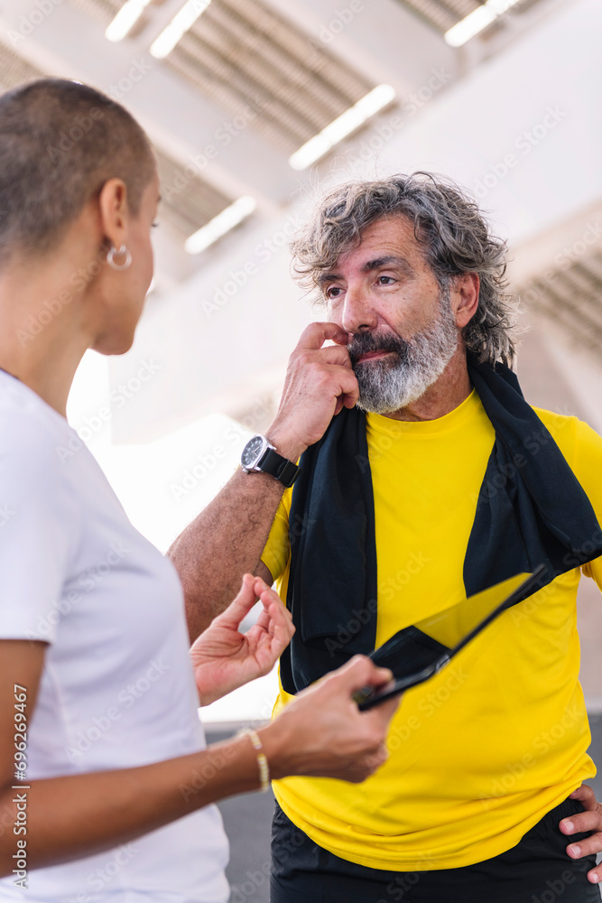 Obraz premium senior sports man watching progress of his workout on a tablet and discussing the results with his personal trainer, concept of healthy and active lifestyle