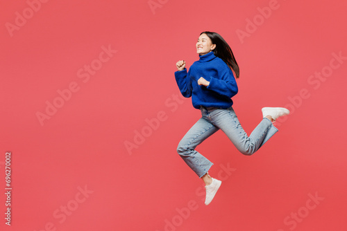 Full body side view happy young woman of Asian ethnicity she wearing blue sweater casual clothes jump high run fast isolated on plain pastel light pink background studio portrait. Lifestyle concept. photo