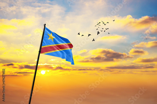 Waving flag of DR Congo against the background of a sunset or sunrise. DR Congo flag for Independence Day. The symbol of the state on wavy fabric.