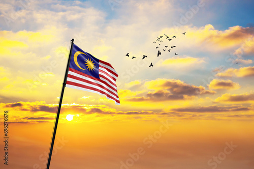 Waving flag of Malaysia against the background of a sunset or sunrise. Malaysia flag for Independence Day. The symbol of the state on wavy fabric.