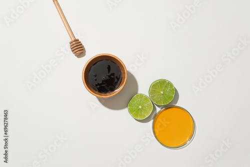 Wooden bowl and petri dish hold honey, accompanied by fresh lemon and honey drizzle on a white background. Embracing natural ingredients in a healthcare-inspired composition.