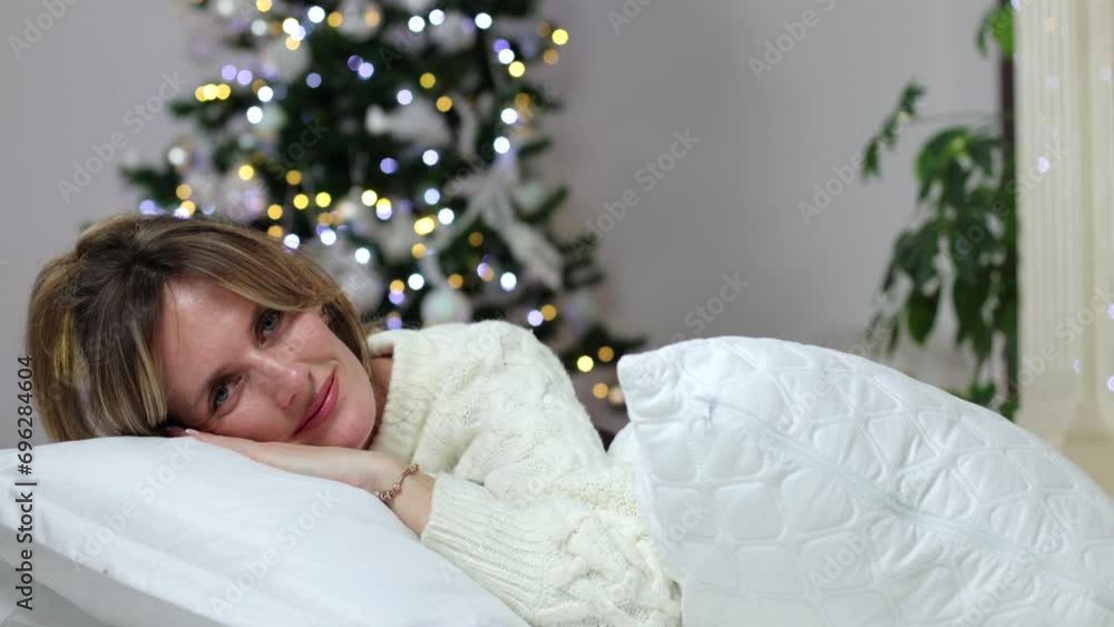 The girl lies on white pillows, against the background of a Christmas tree. Festive atmosphere. New Year at home. Christmas celebration, beautiful slender woman with makeup. The girl lies on white pillows, against the background of a Christmas tree. Festive atmosphere. New Year at home. Christmas celebration, beautiful slender woman with makeup.